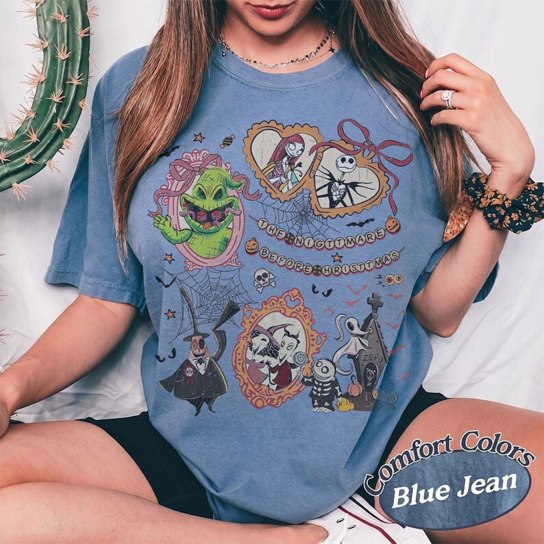 May include: Blue jean colored t-shirt featuring characters from The Nightmare Before Christmas. The shirt has a graphic design with images of Jack Skellington, Sally, Oogie Boogie, and Zero. The text "The Nightmare Before Christmas" is also visible.