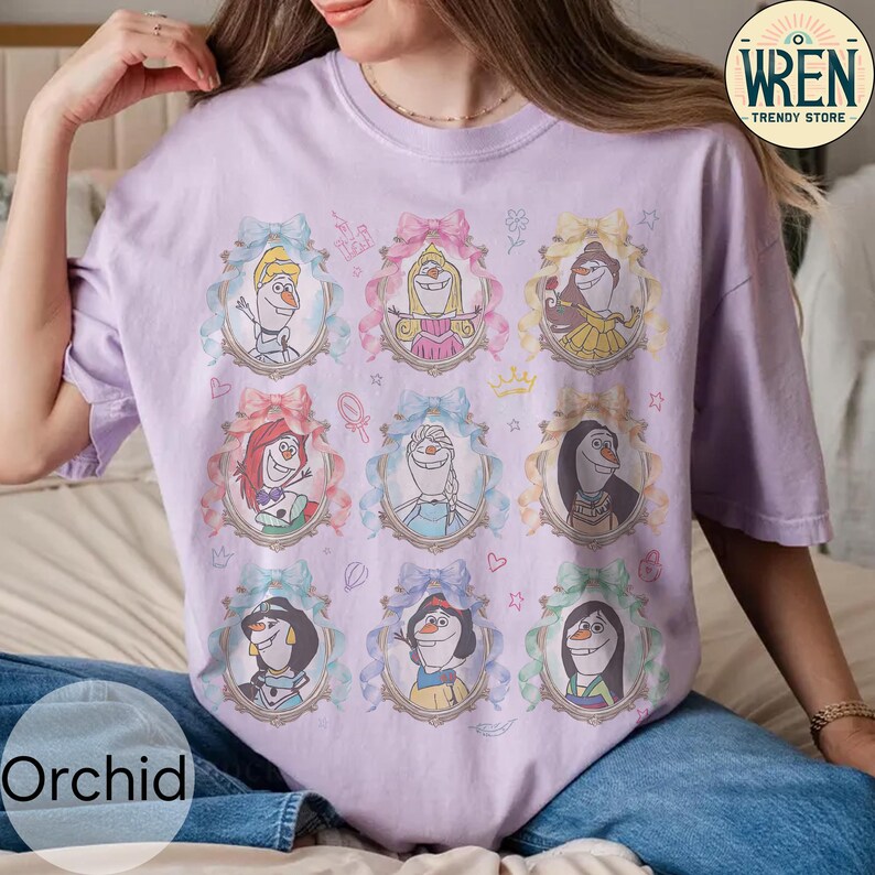 Puede incluir: Una camiseta de color lila claro con nueve retratos enmarcados de personajes animados. Cada retrato est&aacute; rodeado por un marco decorativo con un lazo. La palabra "Orchid" est&aacute; impresa en la parte inferior izquierda de la camiseta.