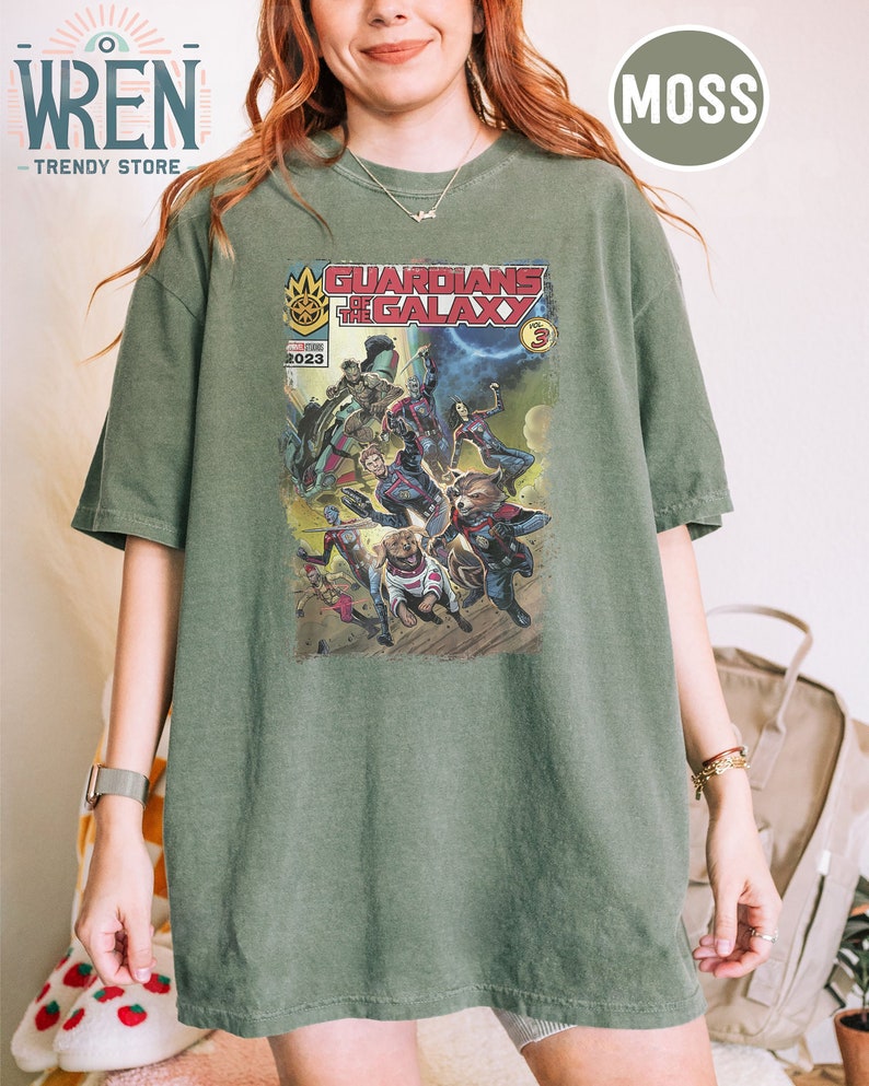 Pu&ograve; includere: Una maglietta verde con una grafica in stile fumetto dei Guardiani della Galassia. La grafica presenta i personaggi del film, tra cui Star-Lord, Gamora, Drax, Rocket e Groot. Il testo "Guardians of the Galaxy Vol. 3" &egrave; stampato sulla grafica.