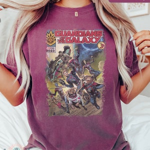 Pu&ograve; includere: Una t-shirt color granata con un design di fumetto vintage con i Guardiani della Galassia. La copertina del fumetto recita "Guardians of the Galaxy Vol. 3" e "Marvel Comics 2023".