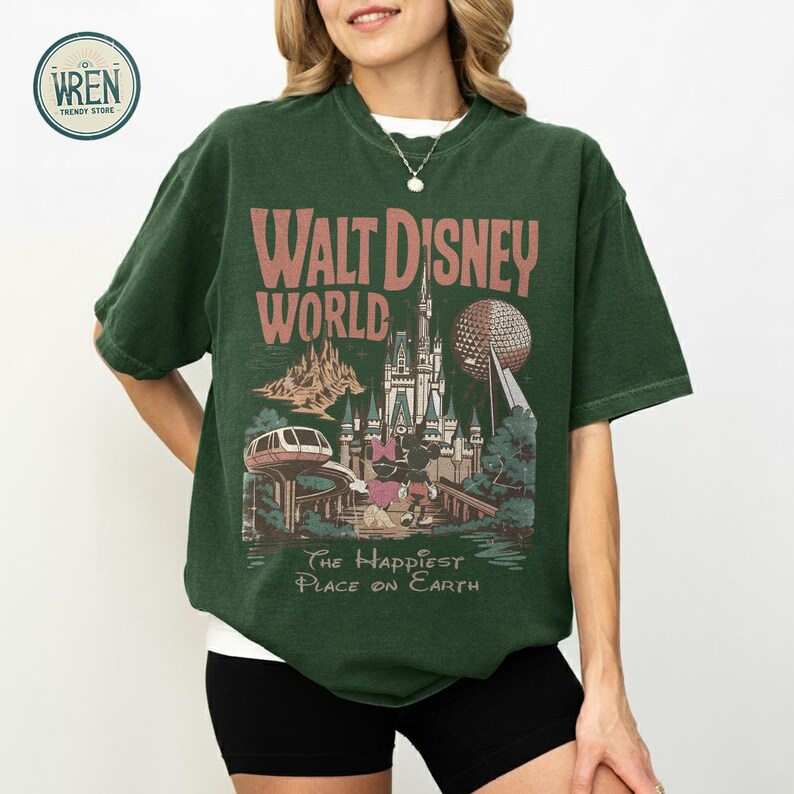 Może przedstawiać: Ciemnozielona koszulka z grafiką w stylu vintage z Walt Disney World. Projekt zawiera nazwę parku, zamek, Spaceship Earth i frazę "The Happiest Place on Earth."