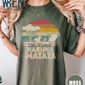 May include: A green t-shirt with a vintage sunset graphic featuring a lion, zebra, and warthog. The text "Hakuna Matata" is printed below the graphic.