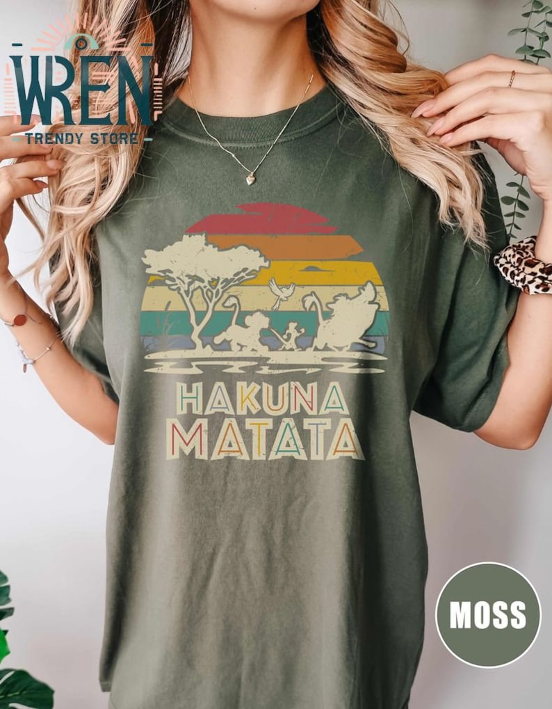 May include: A green t-shirt with a vintage sunset graphic featuring a lion, zebra, and warthog. The text "Hakuna Matata" is printed below the graphic.