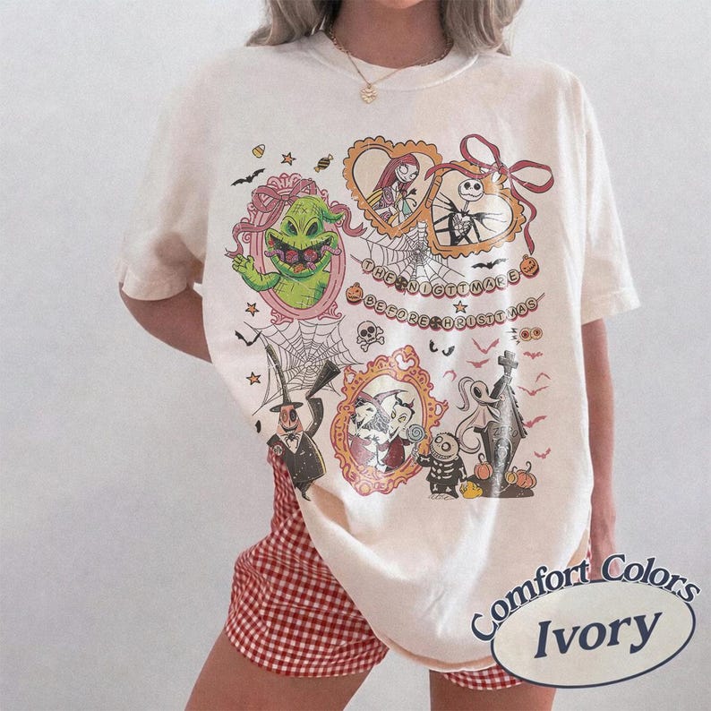May include: Ivory-colored t-shirt featuring a graphic design with characters from "The Nightmare Before Christmas." The design includes images of Jack Skellington, Sally, and Oogie Boogie, with the text "The Nightmare Before Christmas."