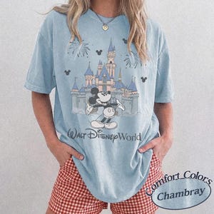 May include: Light blue t-shirt featuring a graphic of Mickey Mouse in front of Cinderella's castle at Walt Disney World. The shirt has a crew neck and short sleeves. The text "Walt Disney World" is printed below the graphic.