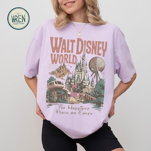 Może przedstawiać: Jasnofioletowa koszulka z grafiką Walt Disney World. Projekt zawiera tekst "Walt Disney World" i "The Happiest Place on Earth", a także ilustracje zamku, Spaceship Earth i innych atrakcji parku.