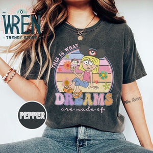 Puede incluir: Una camiseta negra con un gr&aacute;fico de estilo vintage que presenta a una ni&ntilde;a de dibujos animados con una diadema de orejas de Mickey Mouse sosteniendo un cono de helado. El gr&aacute;fico dice "This is what dreams are made of".
