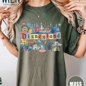 May include: A green t-shirt with a graphic print of the Disneyland Resort logo and various attractions. The text "Disneyland Resort" is printed in colorful letters.