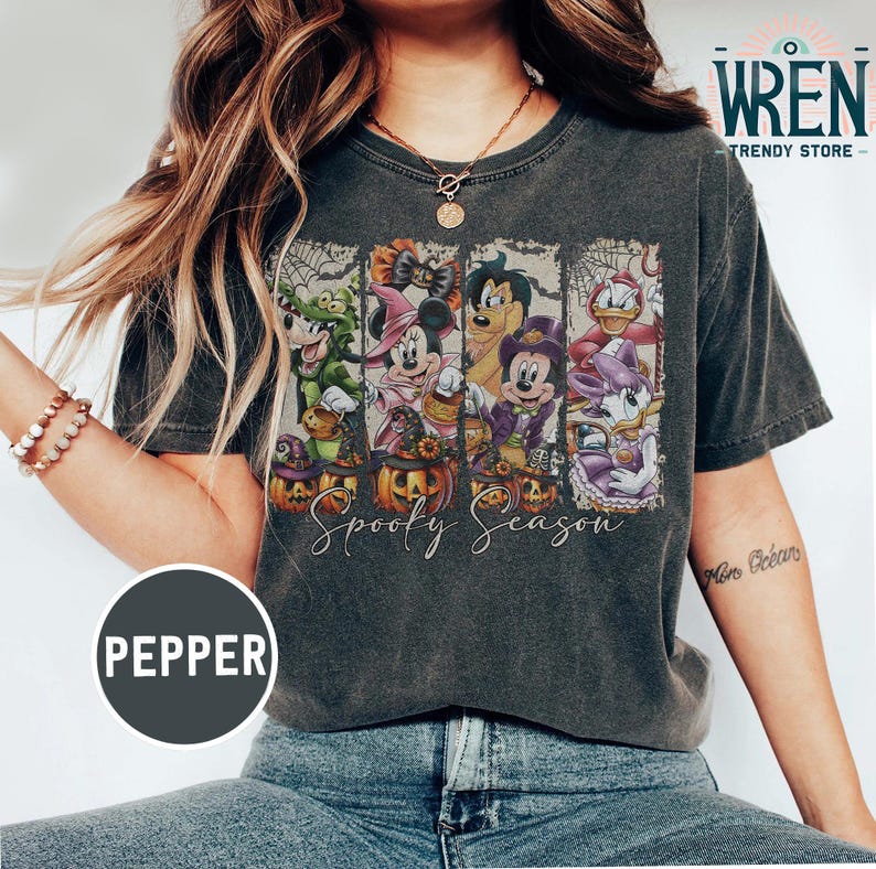 May include: Dark gray t-shirt featuring a Halloween-themed graphic with cartoon characters, pumpkins, and the text "Spooky Season." The design includes characters like Mickey Mouse and Donald Duck in Halloween costumes. The shirt has a vintage, worn look.