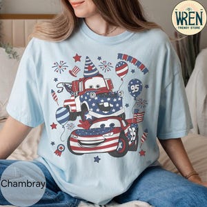 Puede incluir: Camiseta azul claro con un dise&ntilde;o gr&aacute;fico de coches de dibujos animados decorados con dise&ntilde;os de la bandera americana, fuegos artificiales y globos. El dise&ntilde;o incluye el n&uacute;mero 95 y estrellas patri&oacute;ticas. La camiseta es holgada.