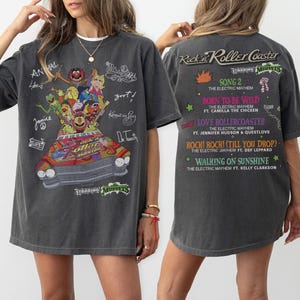 May include: Charcoal grey t-shirt with a vibrant Muppets graphic on the front, and song titles from "Rock n Roller Coaster" on the back. The front also features character names and signatures in white.