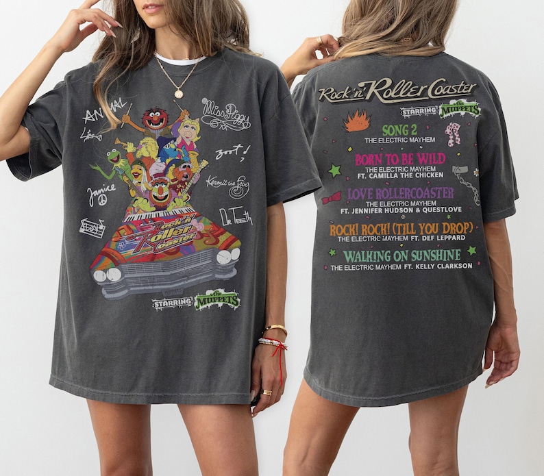 May include: Charcoal grey t-shirt with a vibrant Muppets graphic on the front, and song titles from "Rock n Roller Coaster" on the back. The front also features character names and signatures in white.