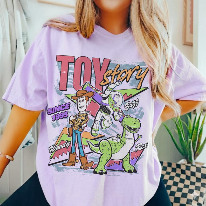 Pode incluir: Uma camiseta lil&aacute;s com um design gr&aacute;fico do filme "Toy Story". O design inclui o texto "Toy Story" e o ano "Desde 1995", juntamente com ilustra&ccedil;&otilde;es de Woody, Buzz Lightyear e Rex, o dinossauro.