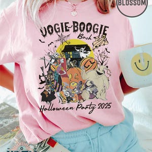Puede incluir: Camiseta rosa claro con un dise&ntilde;o de Halloween que presenta personajes, calabazas y el texto "Vogie Boogie Bash Halloween Party 2025." La camiseta tambi&eacute;n tiene los logotipos "Blossom" y "Wren Trendy Store".
