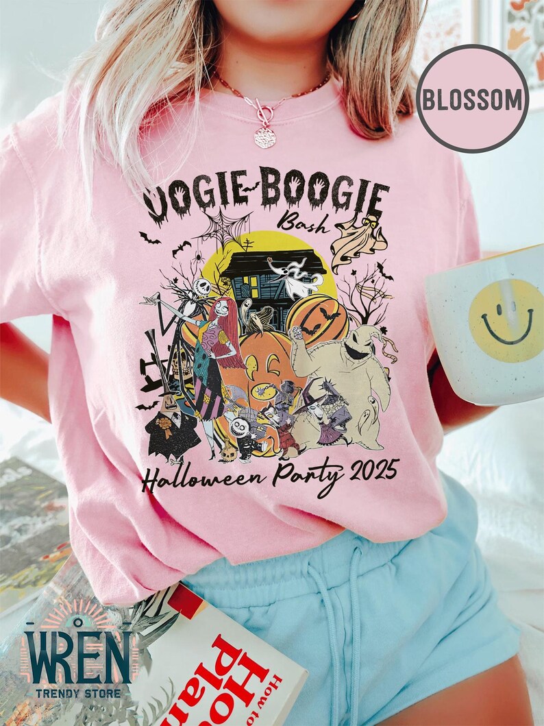 Puede incluir: Camiseta rosa claro con un dise&ntilde;o de Halloween que presenta personajes, calabazas y el texto "Vogie Boogie Bash Halloween Party 2025." La camiseta tambi&eacute;n tiene los logotipos "Blossom" y "Wren Trendy Store".