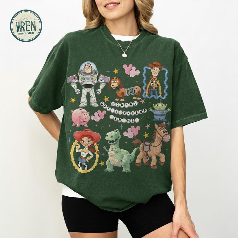 May include: Dark green t-shirt with a print of Toy Story characters, including Buzz Lightyear and Woody. The design features the text "You've Got a Friend in Me" and various cartoon images in a colourful arrangement.