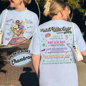 May include: Pale blue t-shirt with a graphic of Muppets characters and the text "Rockin' Roller Coaster". The back of the shirt lists song titles and artist names. The shirt is made of Chambray Comfort Colors.
