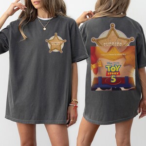 Puede incluir: Una camiseta gris carb&oacute;n con una peque&ntilde;a insignia de estrella de sheriff dorada en el pecho izquierdo. La parte posterior muestra una gran estrella de sheriff dorada sobre un gr&aacute;fico de un torso de personaje con el texto Disney Pixar Toy Story 5.