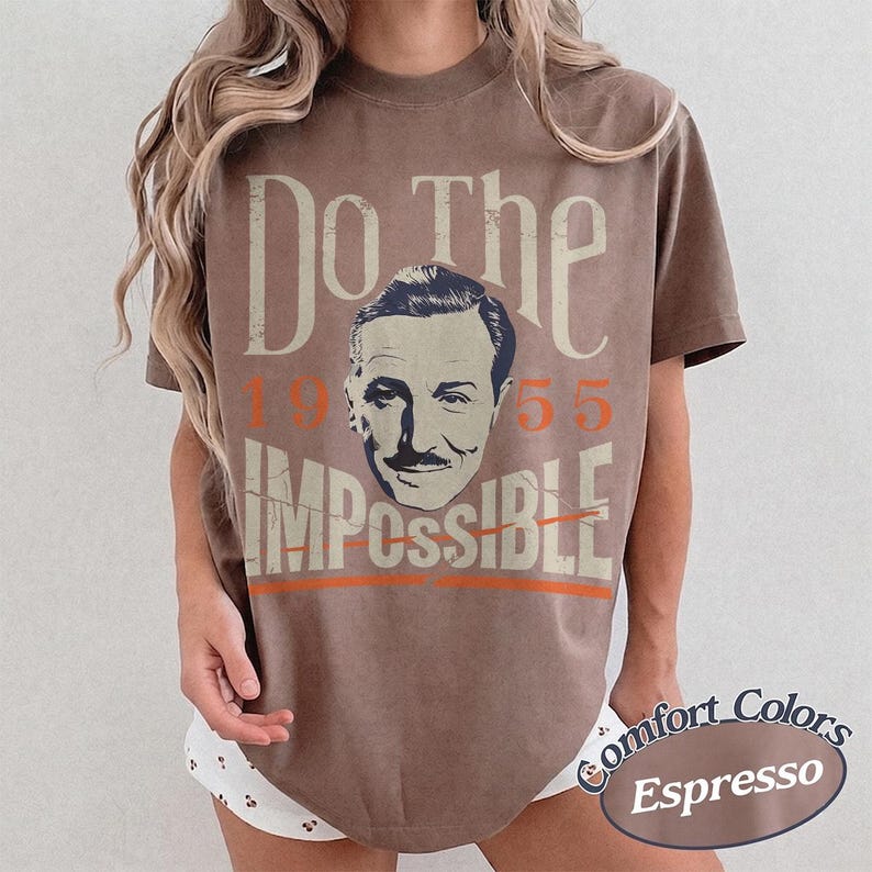 May include: Espresso-colored t-shirt with the text "Do The Impossible" and a portrait of a man. The numbers "1955" are in orange. The shirt is part of the Comfort Colors collection.