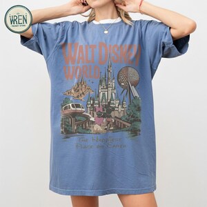 Może przedstawiać: Niebieska koszulka z grafiką w stylu vintage z Walt Disney World. Projekt zawiera zamek, Spaceship Earth, kolejkę jednoszynową oraz Myszki Miki i Minnie. Tekst brzmi "Walt Disney World" i "The Happiest Place on Earth."