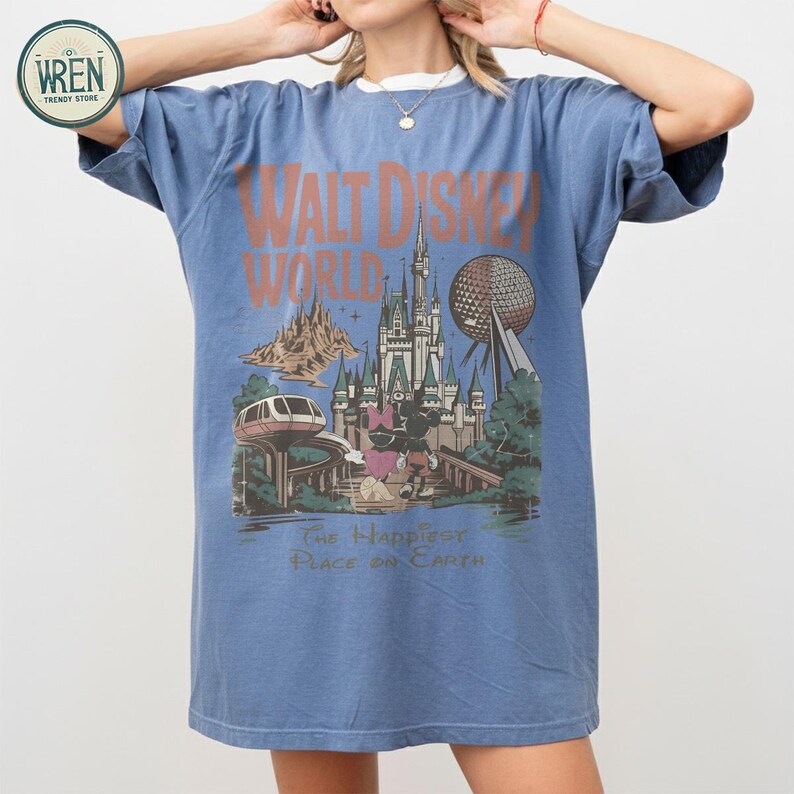 Może przedstawiać: Niebieska koszulka z grafiką w stylu vintage z Walt Disney World. Projekt zawiera zamek, Spaceship Earth, kolejkę jednoszynową oraz Myszki Miki i Minnie. Tekst brzmi "Walt Disney World" i "The Happiest Place on Earth."