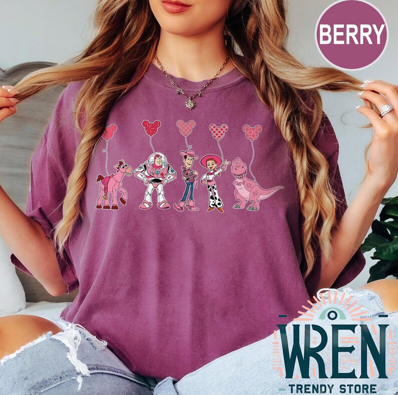Może przedstawiać: Fioletowy T-shirt z grafiką postaci z Toy Story trzymających r&oacute;żowe balony w kształcie serca. Postacie to Woody, Buzz Astral, Jessie, Rex i Bulterier.
