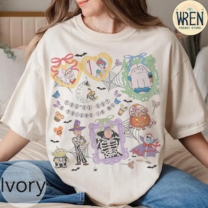 Puede incluir: Camiseta de color marfil con un diseño gráfico colorido con personajes de dibujos animados en marcos, incluyendo un fantasma y un esqueleto. La camiseta tiene el texto "YOU'VE GOT A FRIEND IN ME" y es de WREN Trendy Store.