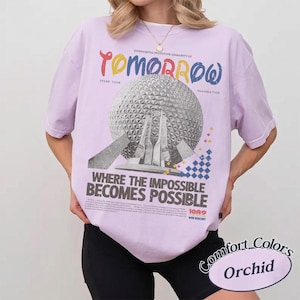 May include: A light purple t-shirt featuring a graphic of a geodesic sphere structure. The text reads: "EXPERIMENTAL PROTOTYPE COMMUNITY OF TOMORROW", "SPARK YOUR IMAGINATION", "WHERE THE IMPOSSIBLE BECOMES POSSIBLE", "1982", and "WALT DISNEY WORLD RESORT".
