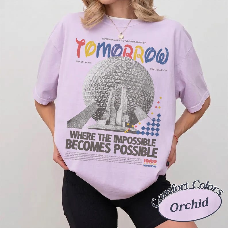 May include: A light purple t-shirt featuring a graphic of a geodesic sphere structure. The text reads: "EXPERIMENTAL PROTOTYPE COMMUNITY OF TOMORROW", "SPARK YOUR IMAGINATION", "WHERE THE IMPOSSIBLE BECOMES POSSIBLE", "1982", and "WALT DISNEY WORLD RESORT".