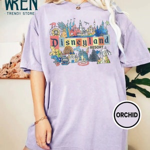 May include: A lavender t-shirt with a colorful graphic of Disneyland Resort attractions and the text "Disneyland Resort".