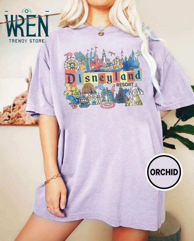 May include: A lavender t-shirt with a colorful graphic of Disneyland Resort attractions and the text "Disneyland Resort".