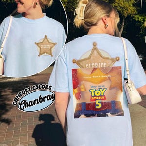 Puede incluir: Una camiseta azul claro con una peque&ntilde;a insignia de estrella de sheriff dorada en el pecho izquierdo. La parte posterior muestra un gr&aacute;fico grande de una estrella de sheriff dorada y un p&oacute;ster de la pel&iacute;cula Toy Story 5 con el texto Disney Pixar Toy Story 5 e I Knew It.