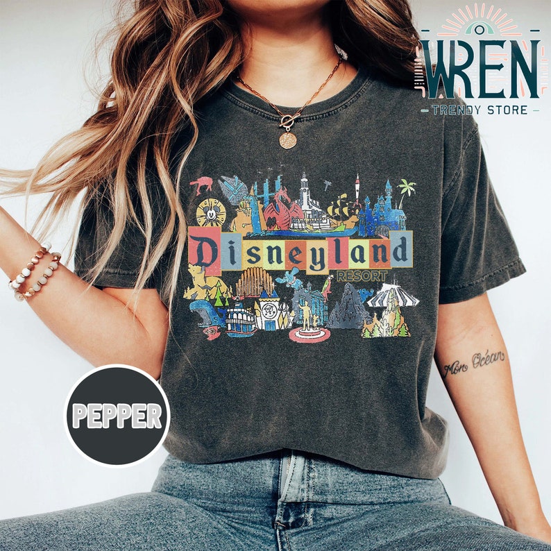 May include: A dark gray t-shirt with a colorful graphic of Disneyland Resort. The graphic includes the text "Disneyland Resort" and various iconic attractions.