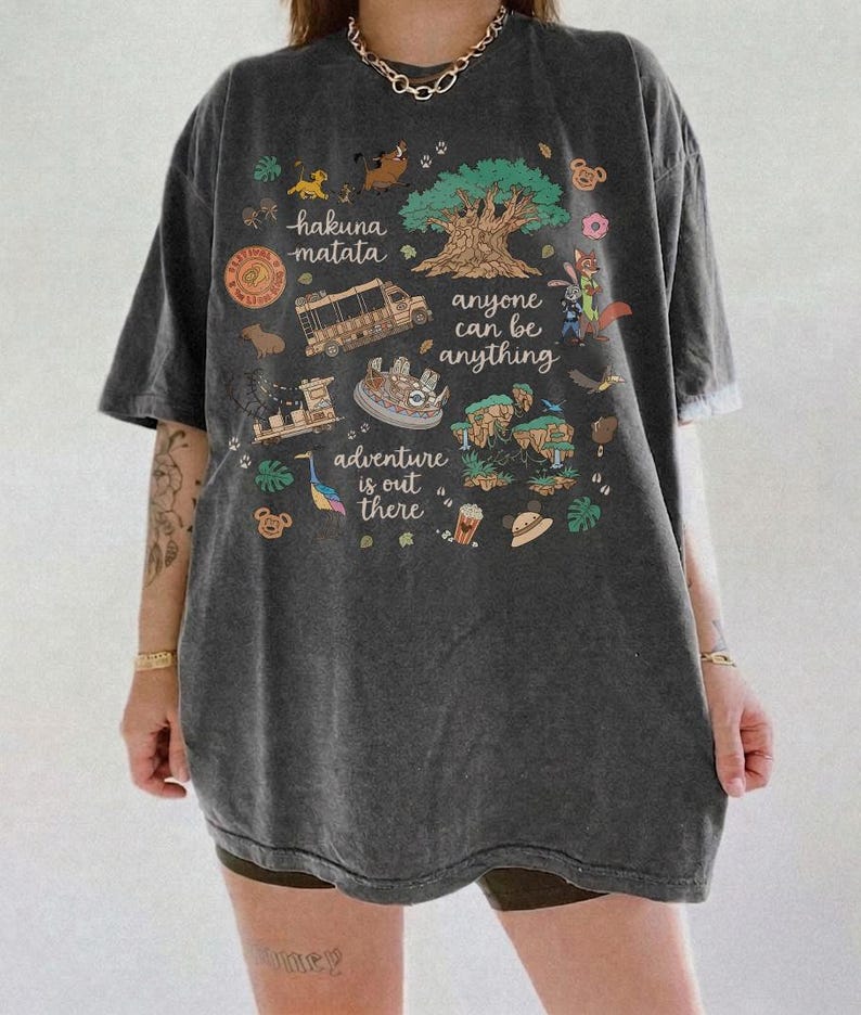 May include: Dark gray t-shirt with a colorful graphic featuring the text "hakuna matata", "anyone can be anything", and "adventure is out there". The graphic includes illustrations of a tree, animals, and a safari vehicle.