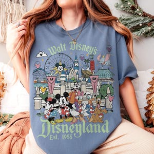 May include: Blue t-shirt featuring a Disneyland graphic with Mickey Mouse, Minnie Mouse, Donald Duck, and other Disney characters. The graphic includes the text "Walt Disney's Disneyland Est. 1955".