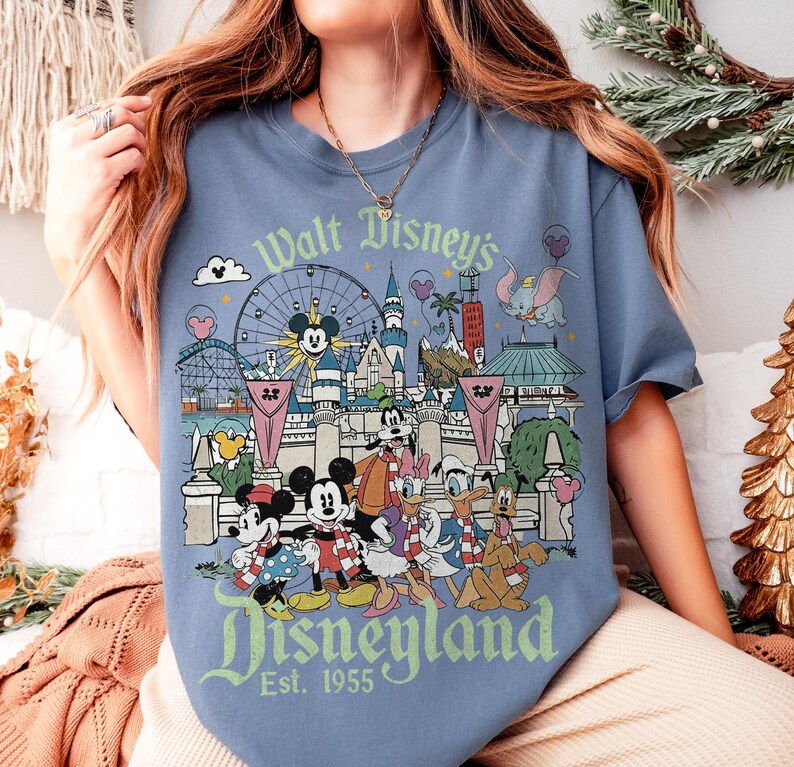 May include: Blue t-shirt featuring a Disneyland graphic with Mickey Mouse, Minnie Mouse, Donald Duck, and other Disney characters. The graphic includes the text "Walt Disney's Disneyland Est. 1955".