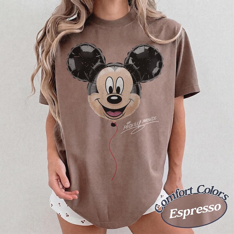 Op de afbeelding: Espresso-kleurig T-shirt met een Mickey Mouse ballonafbeelding. Het ontwerp bevat een lachend Mickey-gezicht met zwarte oren en de tekst "Mickey Mouse". Onderdeel van de Comfort Colors collectie.