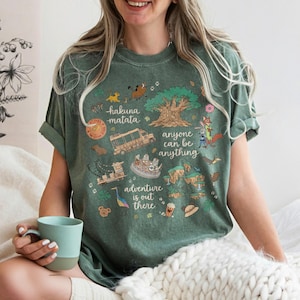 May include: Green t-shirt with a colorful graphic featuring the words "hakuna matata", "anyone can be anything", and "adventure is out there". The design includes cartoon images of animals, a tree, and other themed elements.