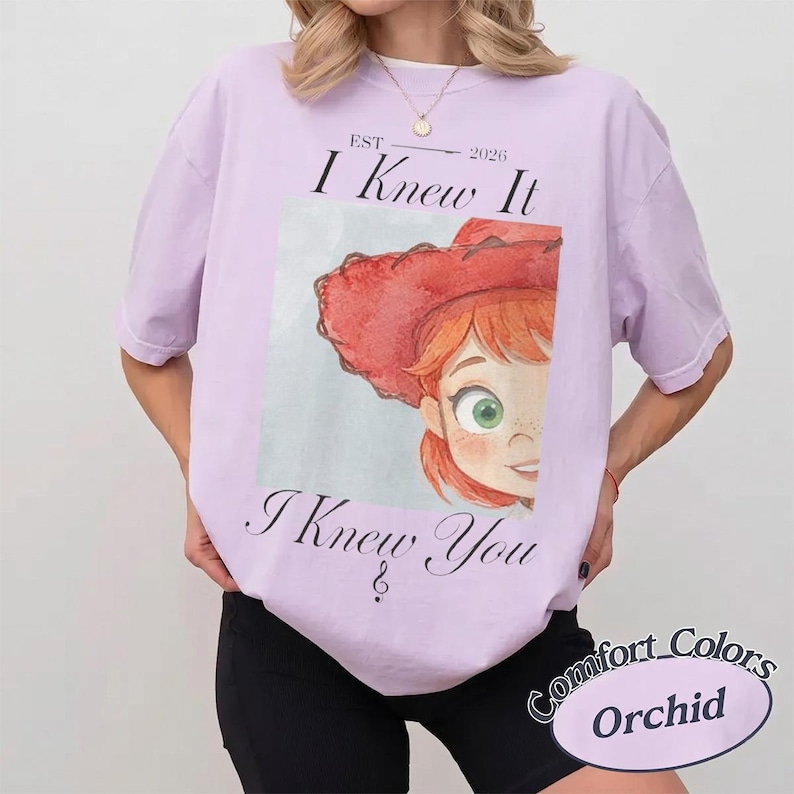 May include: A light purple short-sleeve t-shirt featuring a graphic of a red-haired character wearing a red cowboy hat. The text above reads EST 2026 I Knew It and the text below reads I Knew You. The shirt has a crew neckline and a relaxed fit.