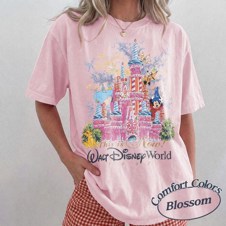Może przedstawiać: Jasnor&oacute;żowa koszulka z grafiką zamku Kopciuszka, Myszki Miki i innych postaci. Pod spodem nadrukowano napis "This is Now! Walt Disney World 1997". Koszulka oznaczona jest jako "Comfort Colors Blossom".