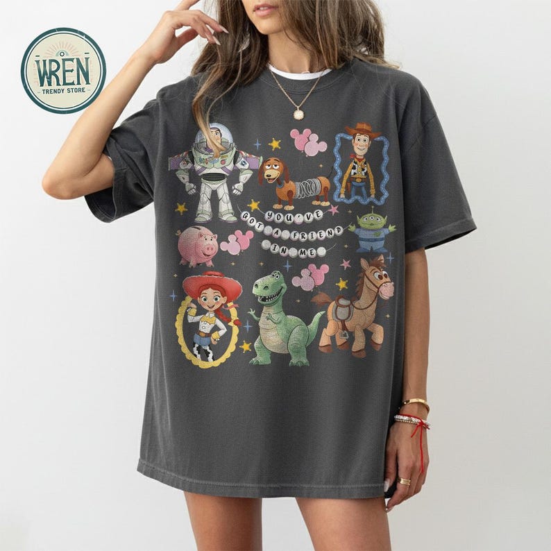 May include: Dark grey t-shirt with colourful Toy Story cartoon characters, including Buzz Lightyear, Woody, Jessie, and Rex. The text "You've Got a Friend in Me" is also visible on the shirt. A fun, casual top.