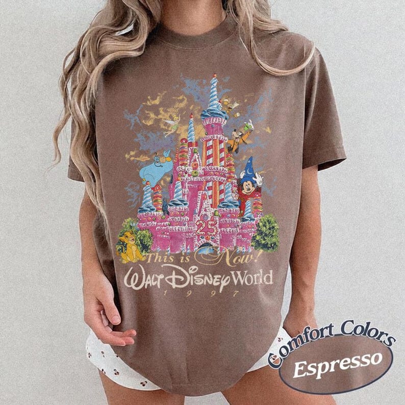Może przedstawiać: Brązowy t-shirt z r&oacute;żową grafiką zamku i napisem "This is Now! Walt Disney World 1997". Grafika zawiera postacie Disneya i liczbę "25". Koszulka jest marki Comfort Colors.