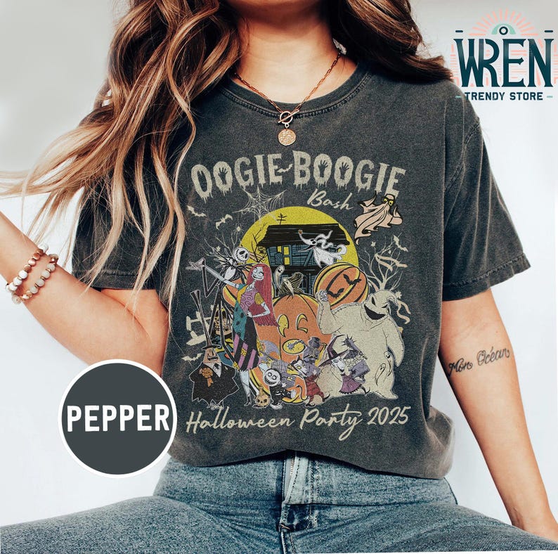 Puede incluir: Camiseta gris oscuro con un gr&aacute;fico colorido de Halloween. El dise&ntilde;o presenta personajes, calabazas y una casa embrujada bajo la luna llena. El texto en la camiseta dice "Oogie Boogie Bash" y "Halloween Party 2025".
