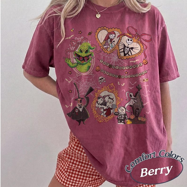 May include: Berry-colored t-shirt featuring characters from "The Nightmare Before Christmas." The design includes framed images of characters like Jack Skellington, Sally, and Oogie Boogie, with the film's title. The shirt has a Comfort Colors label.