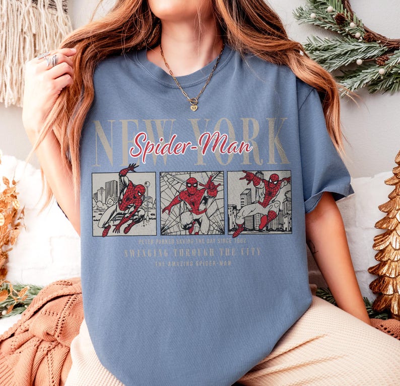 Pu&ograve; includere: Una maglietta blu con una grafica di Spider-Man. Il design include le parole "New York" e "Spider-Man" in un font stilizzato, insieme a pannelli di fumetti di Spider-Man in azione. Il testo aggiuntivo recita "Swinging Through The City."