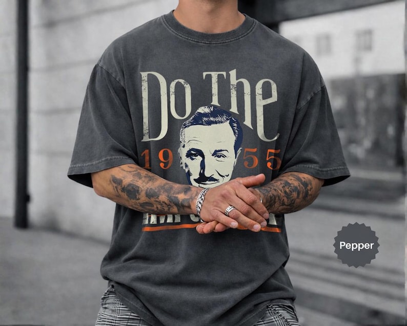 May include: Pepper-colored t-shirt with the text "Do The" above a vintage portrait and the number "1955". The shirt has a distressed look, with a faded design and a crew neck.
