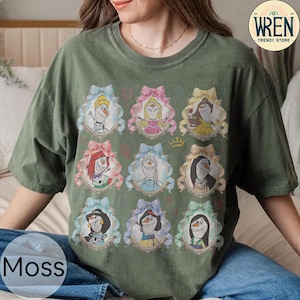 Puede incluir: Camiseta verde musgo con personajes de dibujos animados en marcos adornados con lazos. La camiseta tiene cuello redondo y mangas cortas. La palabra "Moss" est&aacute; impresa en la parte inferior izquierda. La camiseta es de "Wren Trendy Store".
