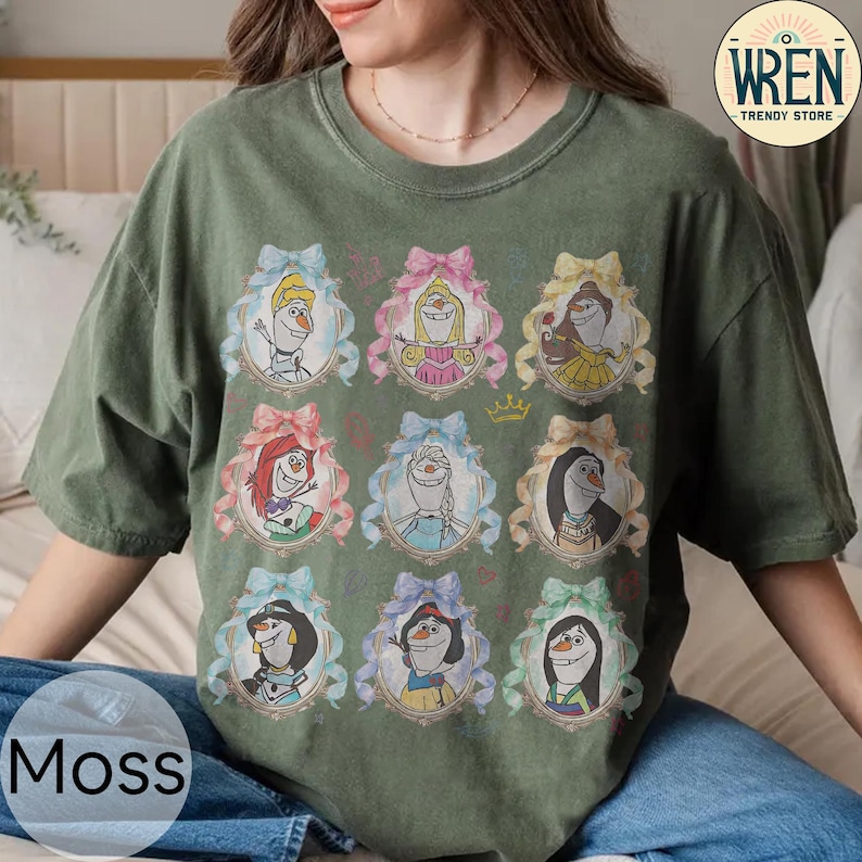 Puede incluir: Camiseta verde musgo con personajes de dibujos animados en marcos adornados con lazos. La camiseta tiene cuello redondo y mangas cortas. La palabra "Moss" est&aacute; impresa en la parte inferior izquierda. La camiseta es de "Wren Trendy Store".