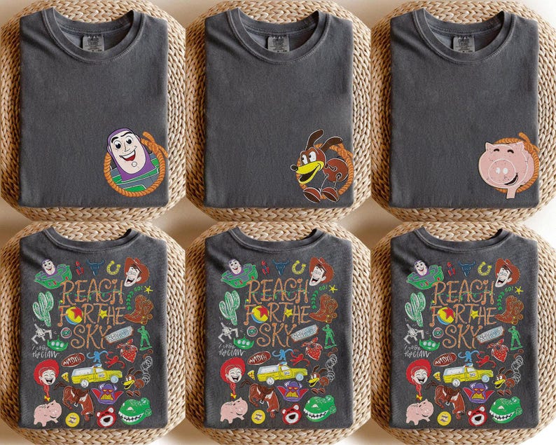 K&ouml;nnte beinhalten: Ein anthrazitfarbenes T-Shirt mit einer kleinen Charaktergrafik auf der linken Brust und einer gro&szlig;en, bunten Collage aus Toy Story-Figuren und Symbolen auf der R&uuml;ckseite, inklusive des Textes "REACH FOR THE SKY" in Western-Schrift.