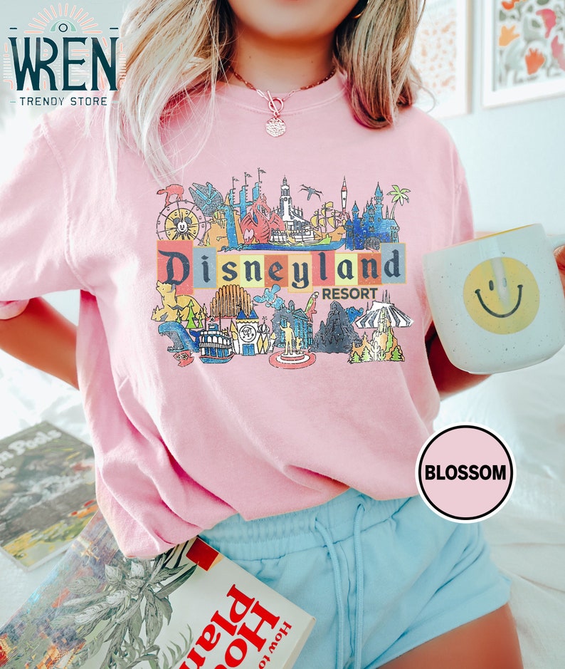 May include: Pink t-shirt with a colorful graphic of the Disneyland Resort logo and various attractions. The graphic includes the text "Disneyland Resort".